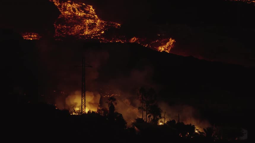Lava flows as fire burning at base of hill silhouettes utility poles