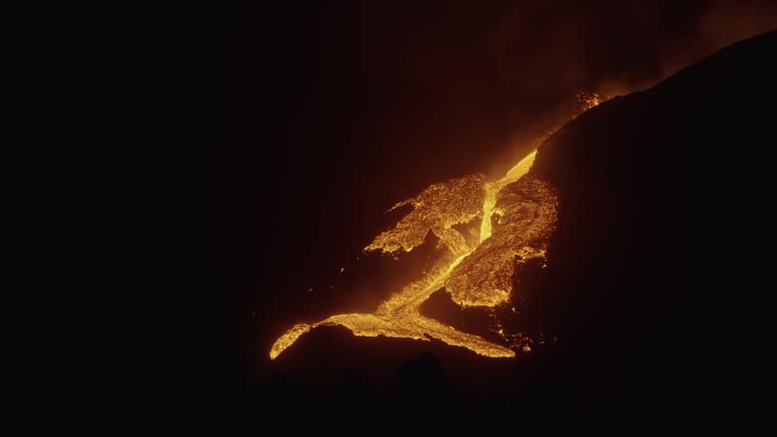 A river of lava glows brightly in the darkness as it flows downhill