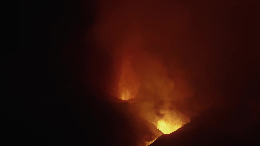 Orange volcano lava flames and smoke rising up from mountain at night