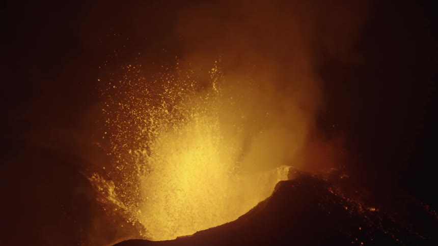 Hot magma glows as a volcano erupts and lava flies into the air