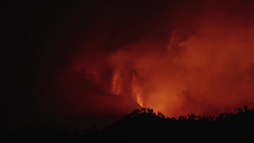 A volcano erupts and spews lava and smoke into the night sky