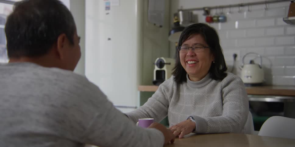 A man and woman laugh and hold hands in a kitchen