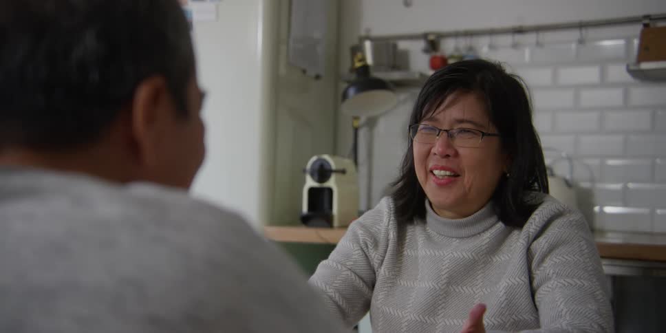 A woman talking to a man sitting in the kitchen