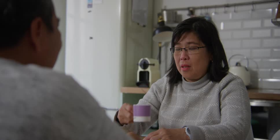 A woman with glasses is talking to someone in front of her and drinks something from a mug