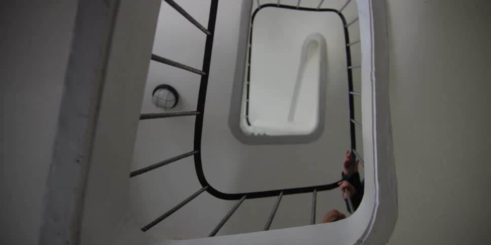 A highangle view of people climbing a white spiral staircase with black handrails