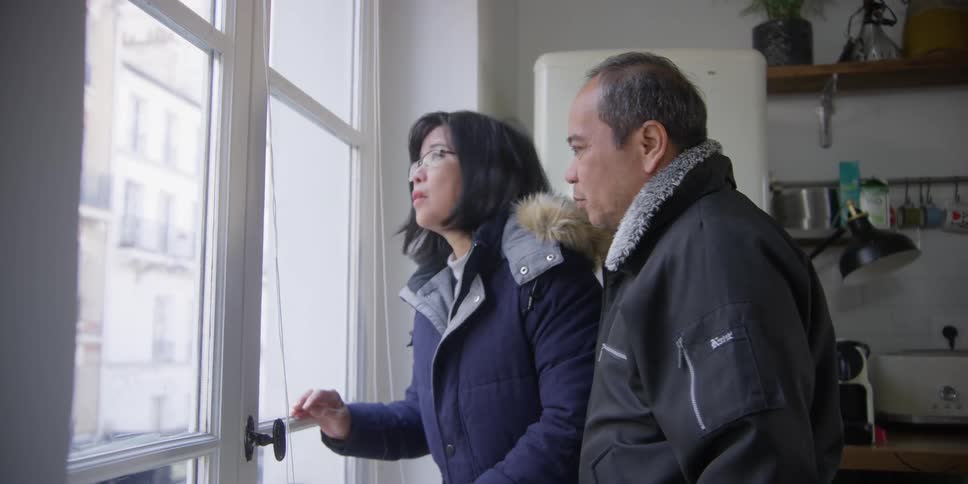 A woman and a man watching the city through their apartment window