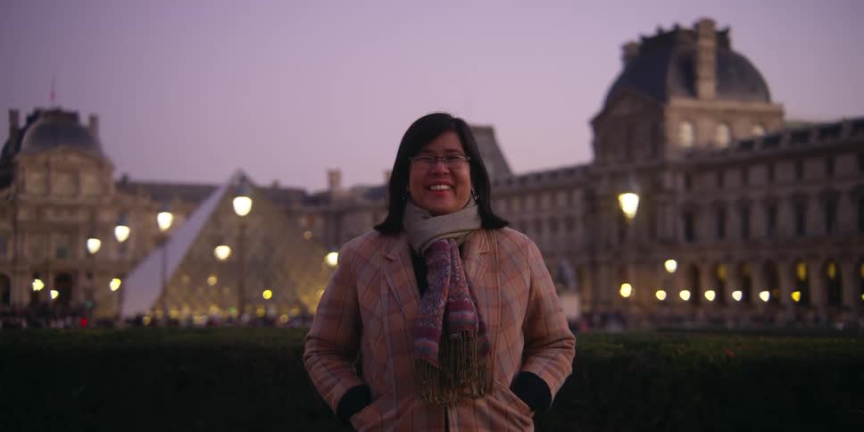 A woman is standing in front of the louvre museum in paris during the evening