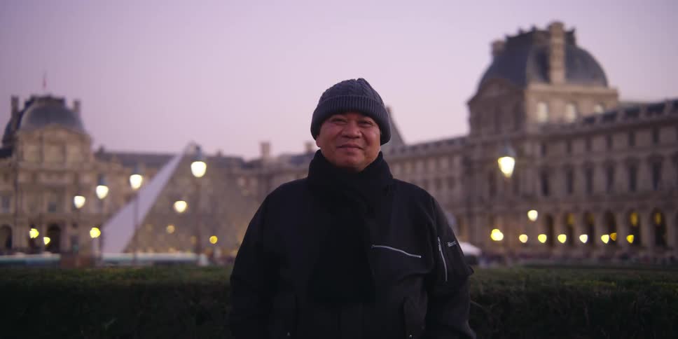 A man is standing in front of the louvre museum in paris during the evening
