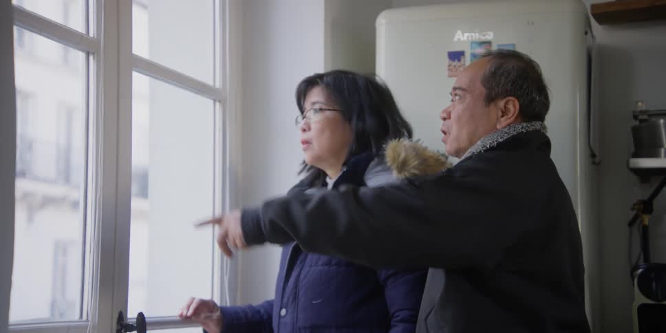 A couple looking out of the apartment window pointing at things of interest
