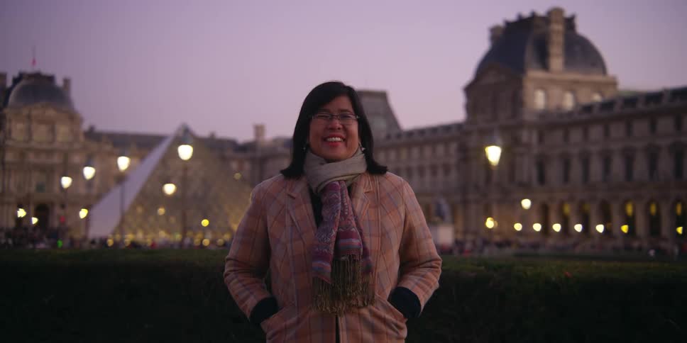 A woman is standing in front of the louvre museum in paris during the evening