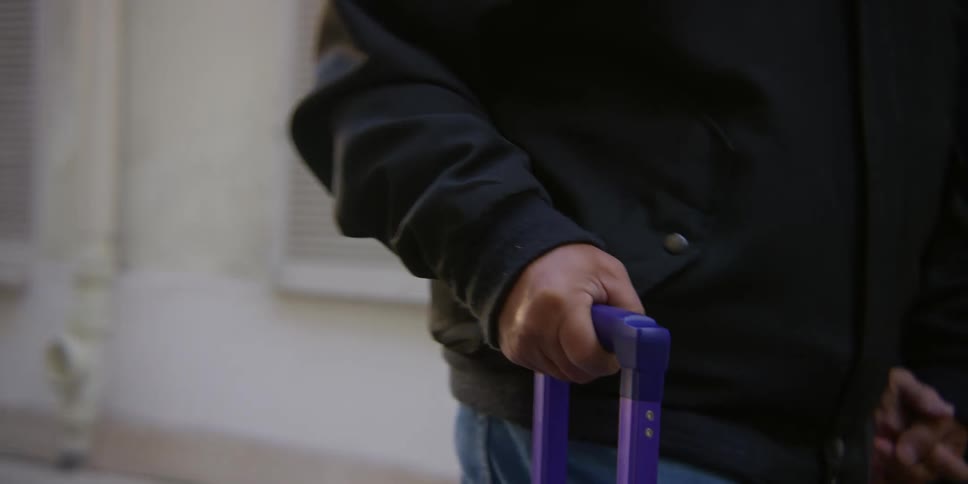 Two people holding hands walking together and pushing a purple suitcase