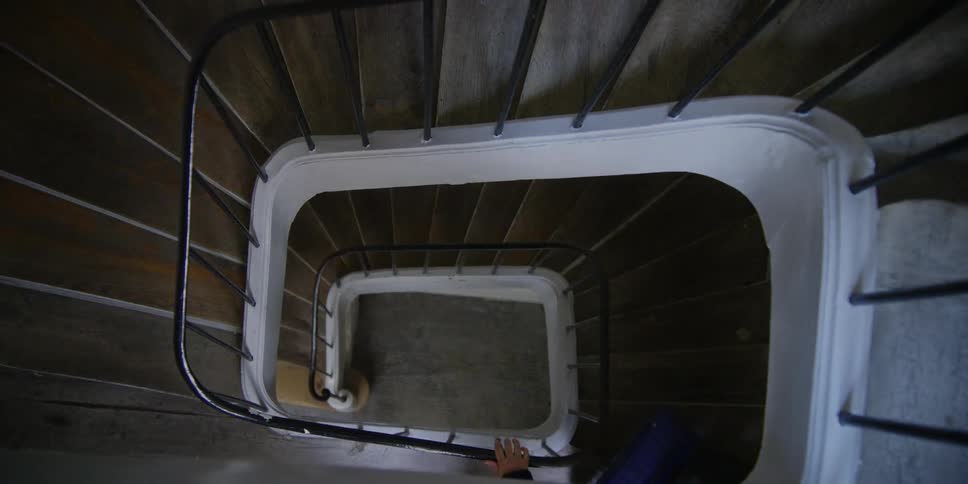 A man and woman gradually ascend a spiraling indoor staircase
