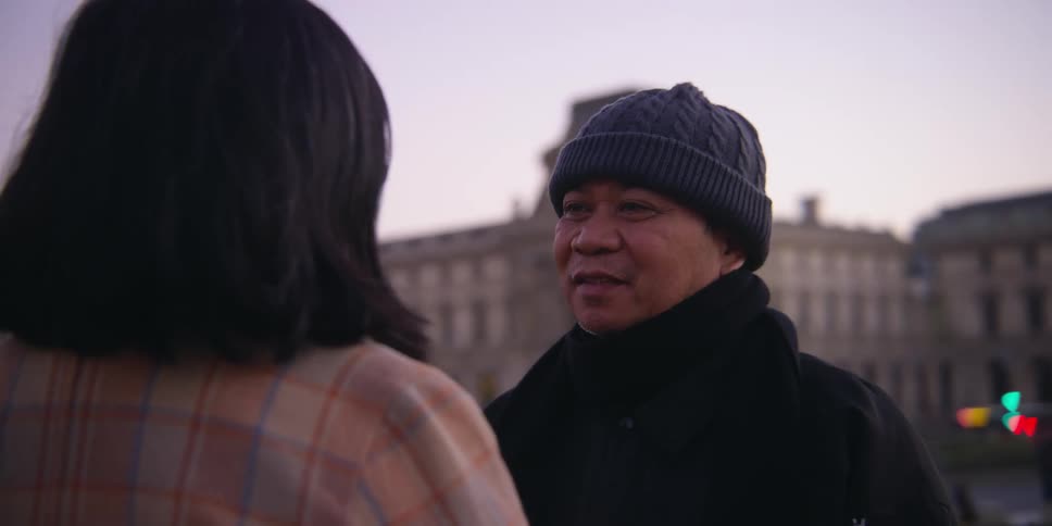 A man stands outdoors talking with his female companion and brushes back her hair
