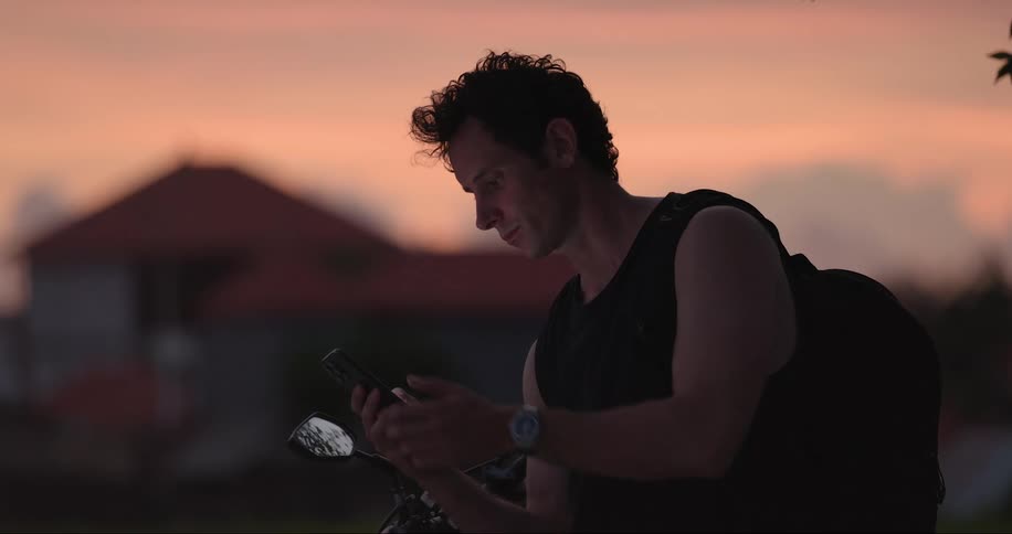 Man sitting on motorcycle at the side of the road consults his smartphone