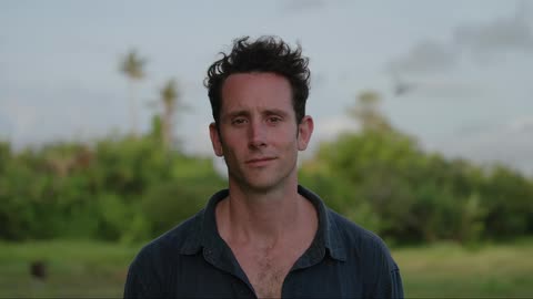 Man smiles slightly while standing outdoors in field during the day