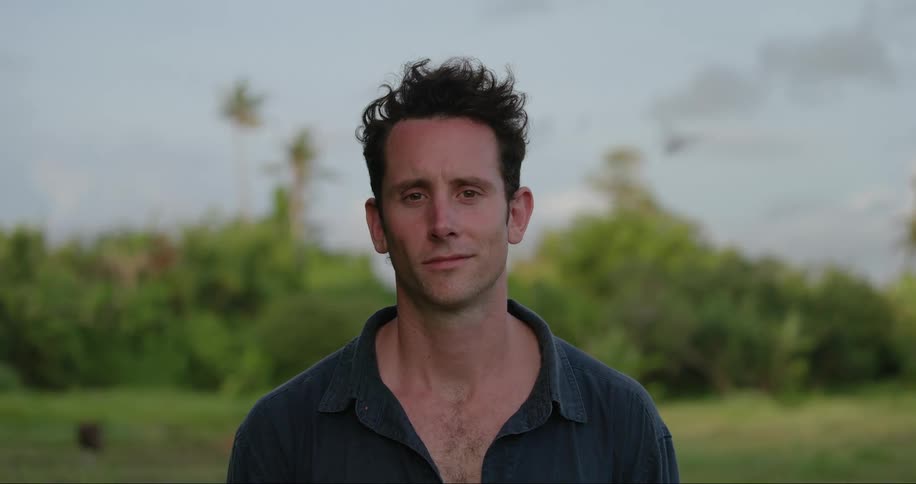 Man smiles slightly while standing outdoors in field during the day