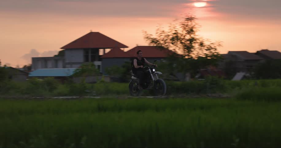 A young guy rides a motorcycle past a group of homes