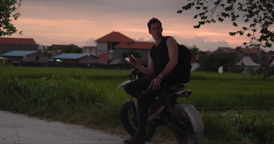 A man sitting on a motorcycle parked in a field in a rural area