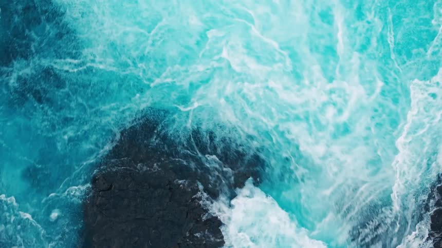 The blue ocean waters crash on the rocks