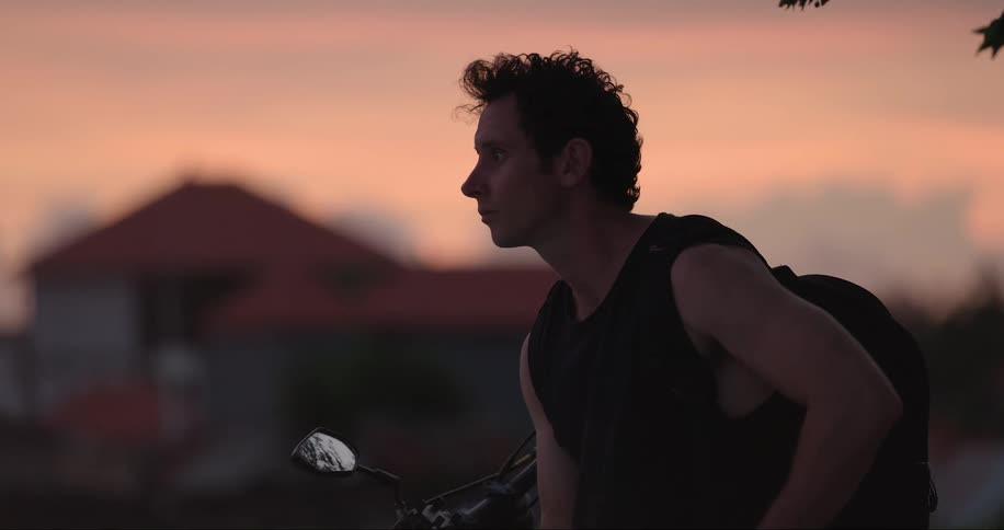 A person walks past a man on a motorcycle using a smart phone