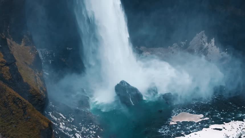A powerful waterfall and a cliff surrounded by snow and mist