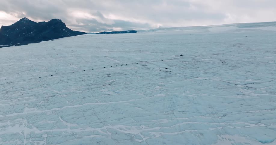 Line of vehicles travels across snow covered plains under an overcast sky