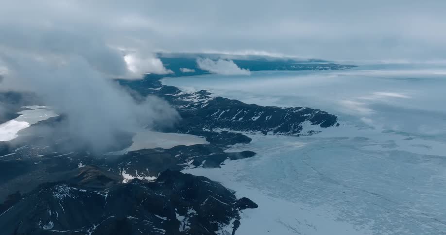 A rocky coastline is adjacent to a frozen layer of ice atop the ocean
