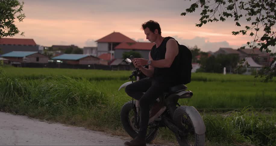 A person sitting on a motorcycle near a grassy field during sunset