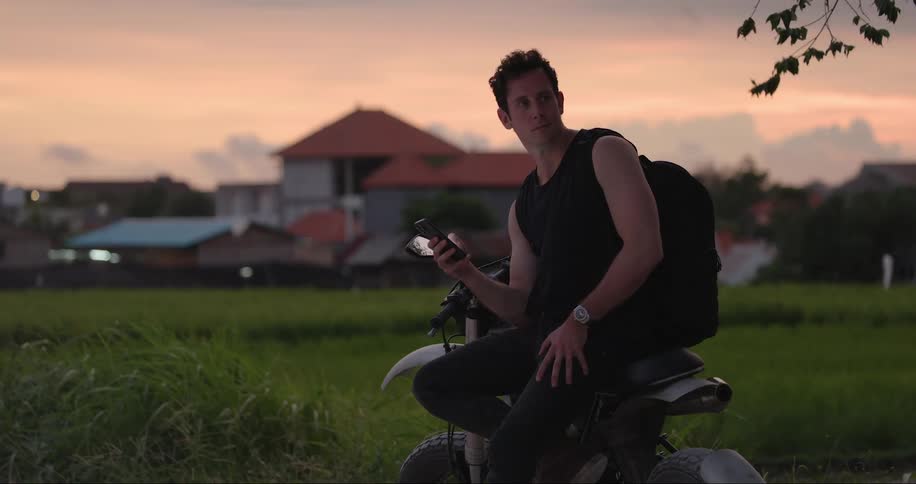 A man seated on a motorcycle smiling while operating a mobile phone outdoor