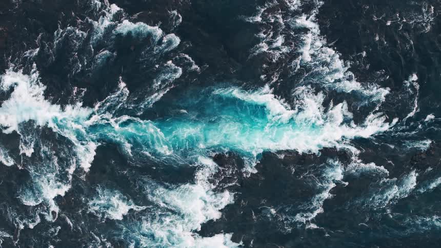 Paler blue water flows among darker water churning past stone islet