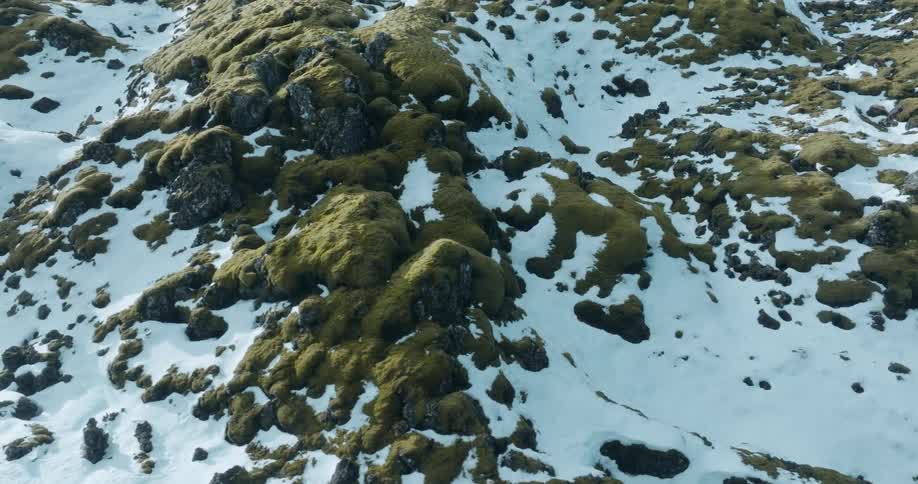Aerial view of greenish rocks surrounded by snow in the mountain slopes