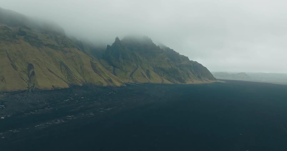 A misty landscape with mountains and dark sand