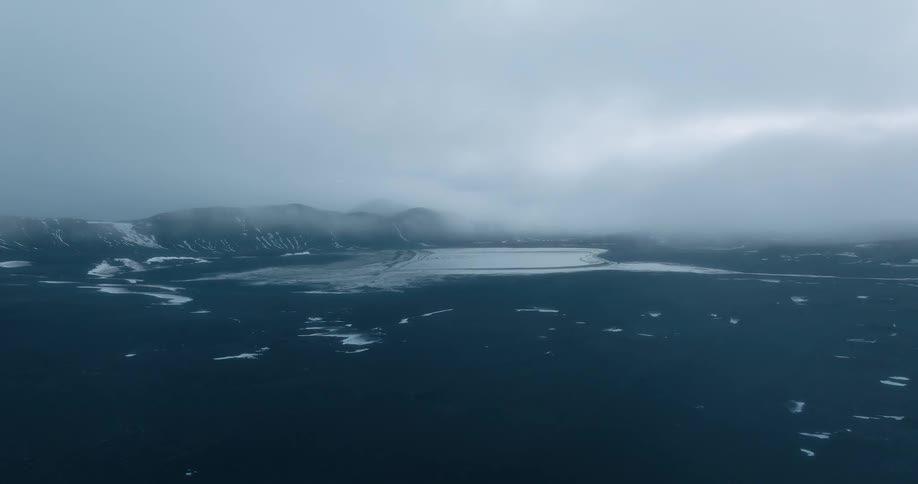Aerial view of dark barren volcanic plains under low clouds