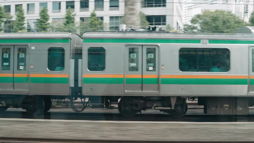 A train with green and orange stripes moving through the city