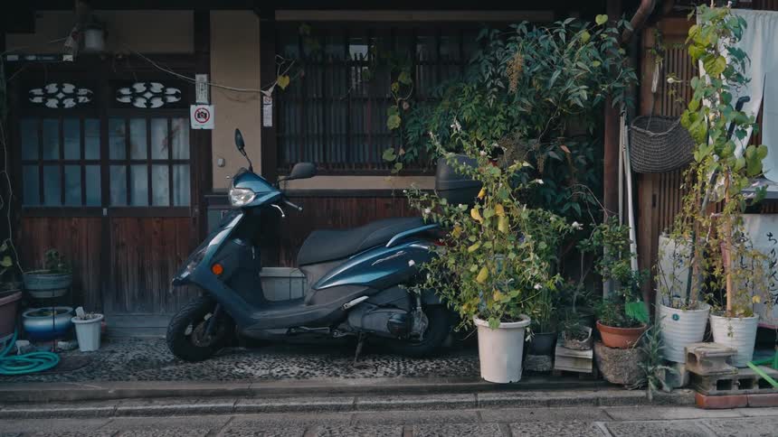A dark colored moped is parked just off the street in front of a building