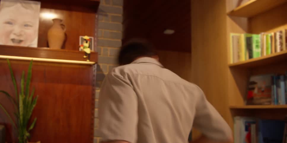 A man doing a dance move is spinning with a cloth in his hand inside a room with several books