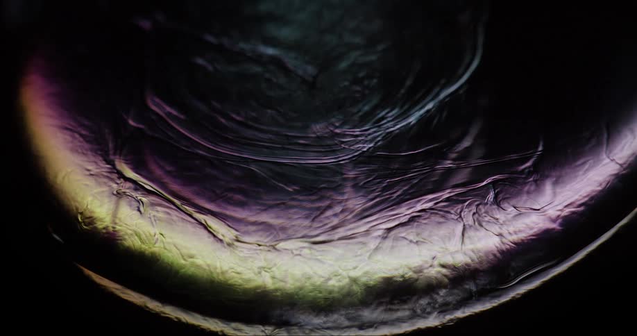 A translucent fluid swirls and flows slowly in a darkened setting