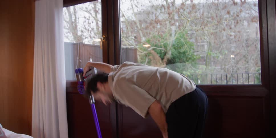 A man has some fun moving his body around while vacuuming the floor
