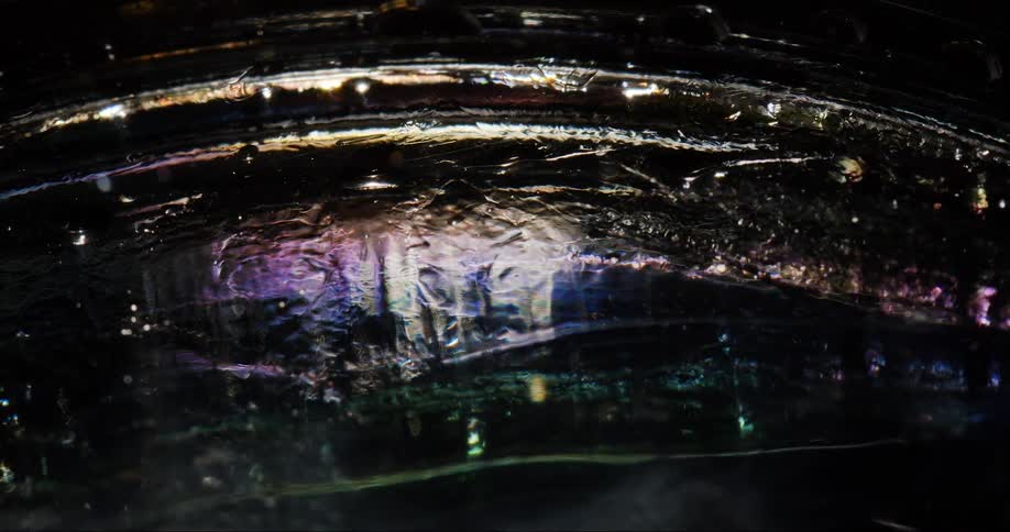 A surface of a liquid is moving and there are some colors reflected on the surface