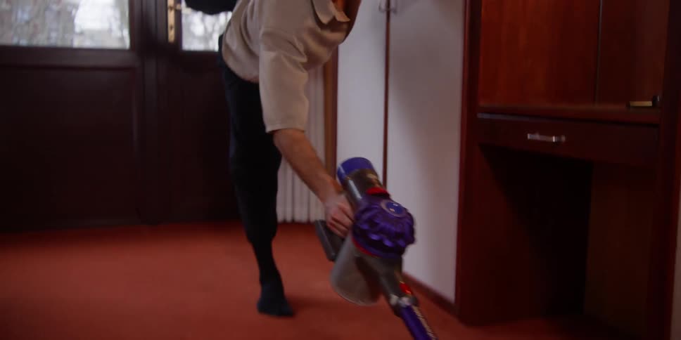 A man dances while cleaning a bedroom with a cordless vacuum