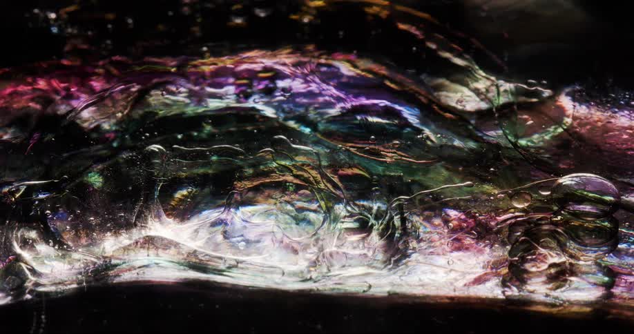 Iridescent bubbles float in multicolored mixture glowing brightly against a dark background