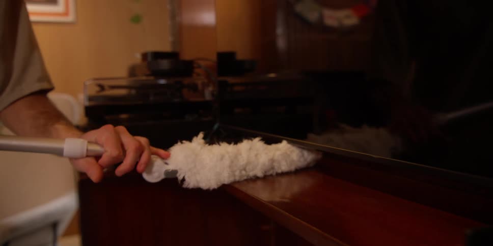 A person using a tool with a cloth on the end cleaning a wooden table