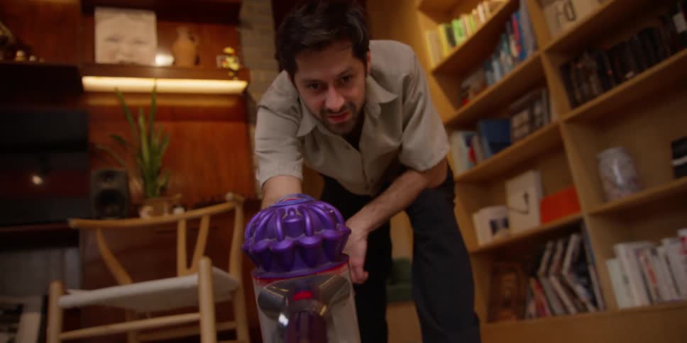 A man cleans a living room with a cordless vacuum