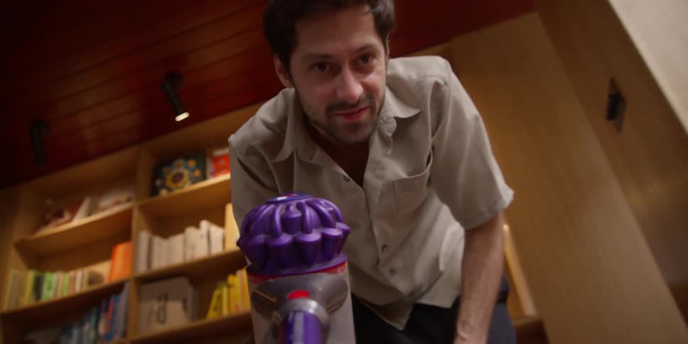 A man is in a living room and is pushing an object with a purple handle