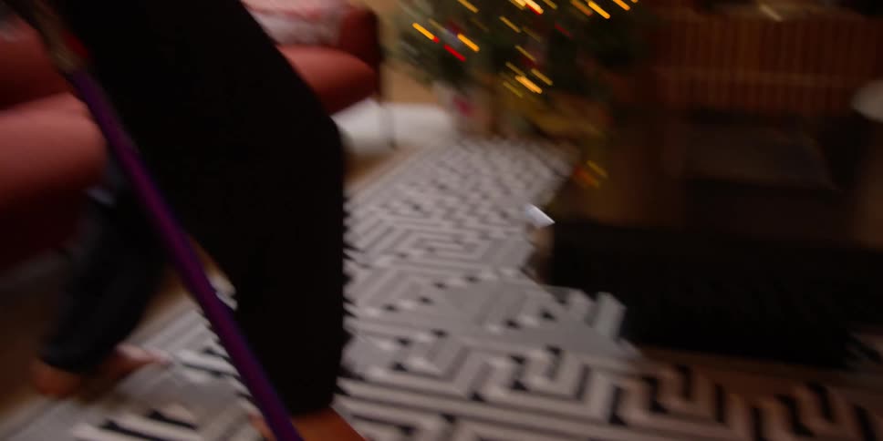 A man gets up from a couch and dances while cleaning a rug with a cordless vacuum