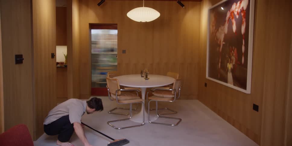 A man is sweeping the house while doing dance moves in a room with wooden walls