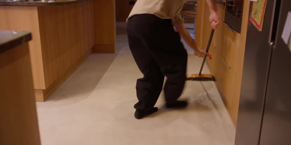 Young man dances while sweeping the floor in an apartment