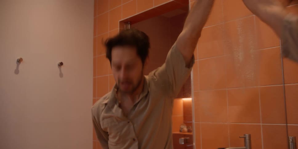 A man is cleaning the mirror in his bathroom