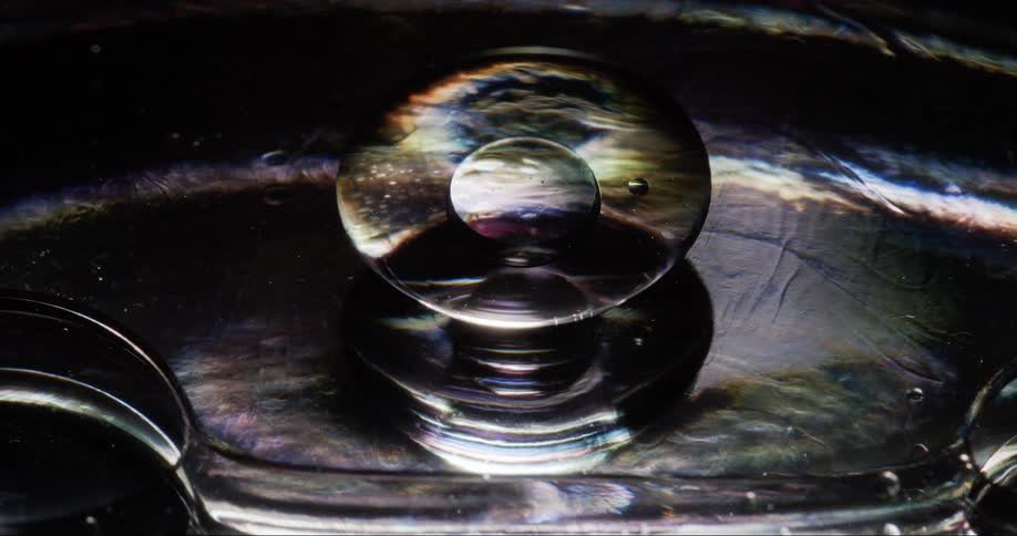 A large bubble in a liquid that is on a black reflective surface