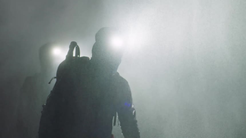 Two people in the middle of a mountain at night on a rainy and snowy day using led headlamps